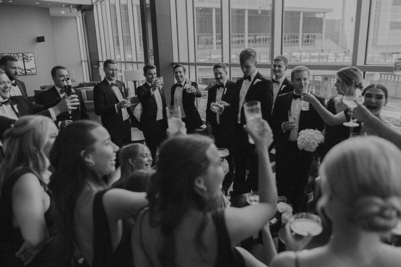 classic black and white bridal party making toast and cheers to new bride and groom. loews hotel in kcmo made for the perfect cocktail hour to have laid back and easy going wedding day