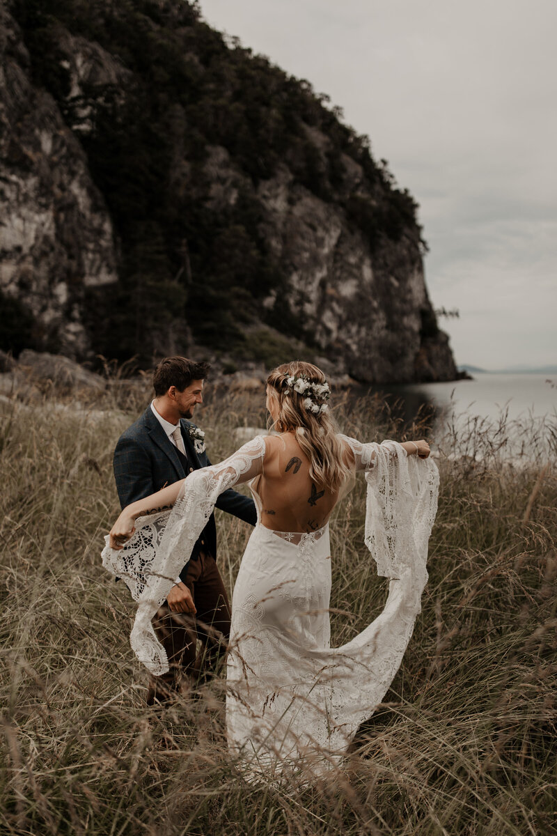 bride and groom dancing in field next to the water