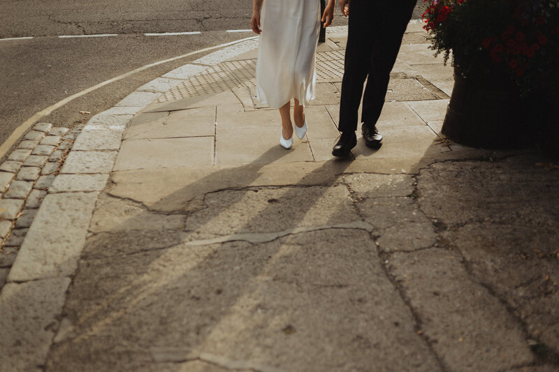 Editorial (hackney london) (city) image of a couple walking side-by-side on a cracked pavement, focusing on wedding attire and street details.