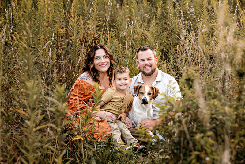 Dad, mom, and toddler son are standing together smiling while standing in front of a mountain backdrop.