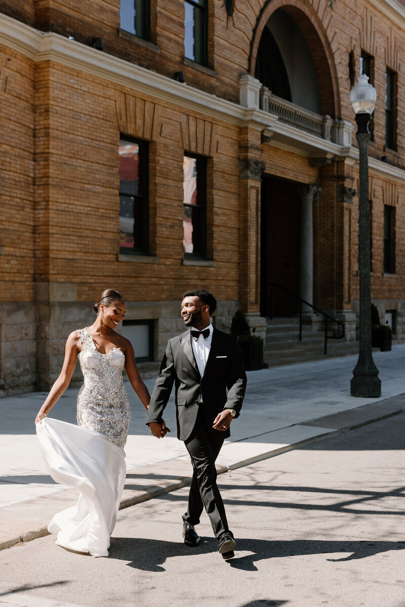 A wedding couple holding hands and walking across a street together 