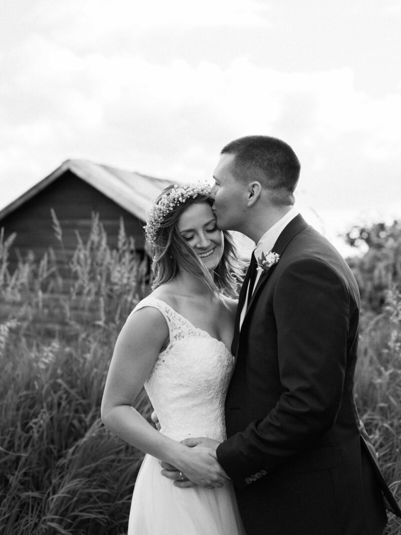 a groom kissing his wife in front of a barn. 