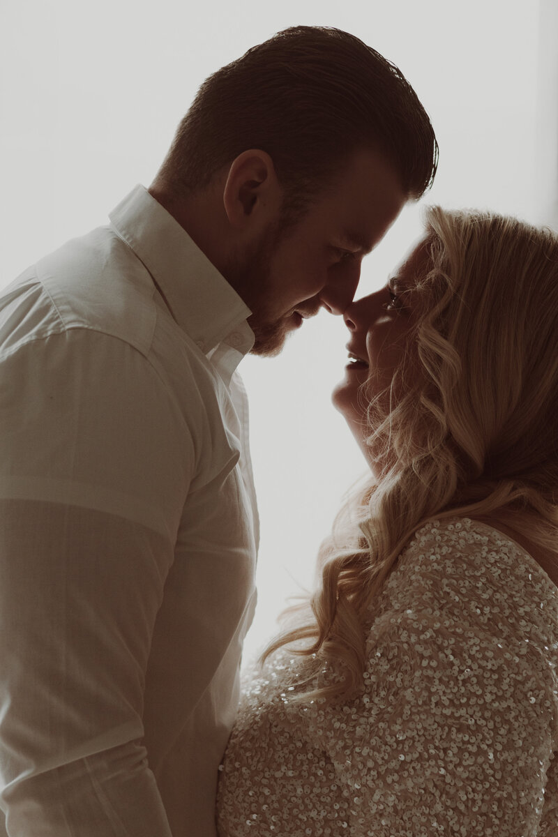 Een man en vrouw kussen voor een raam, omringd door een warme, romantische sfeer.