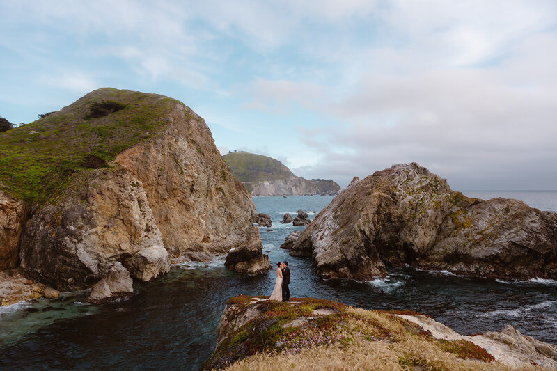 Couple kissing on a cliffside in Big Sur with the ocean in the background.