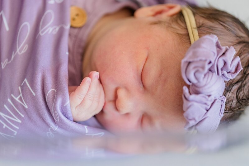 Newborn baby girl holding her hand to her face.