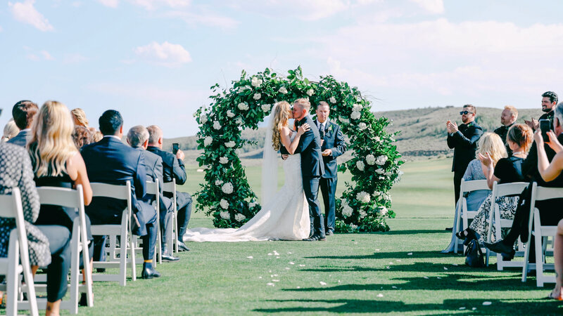 Bride and Groom Kissing at ceremony flower arch on golf course, Promontory club wedding park city utah taken by Cali Warner Media