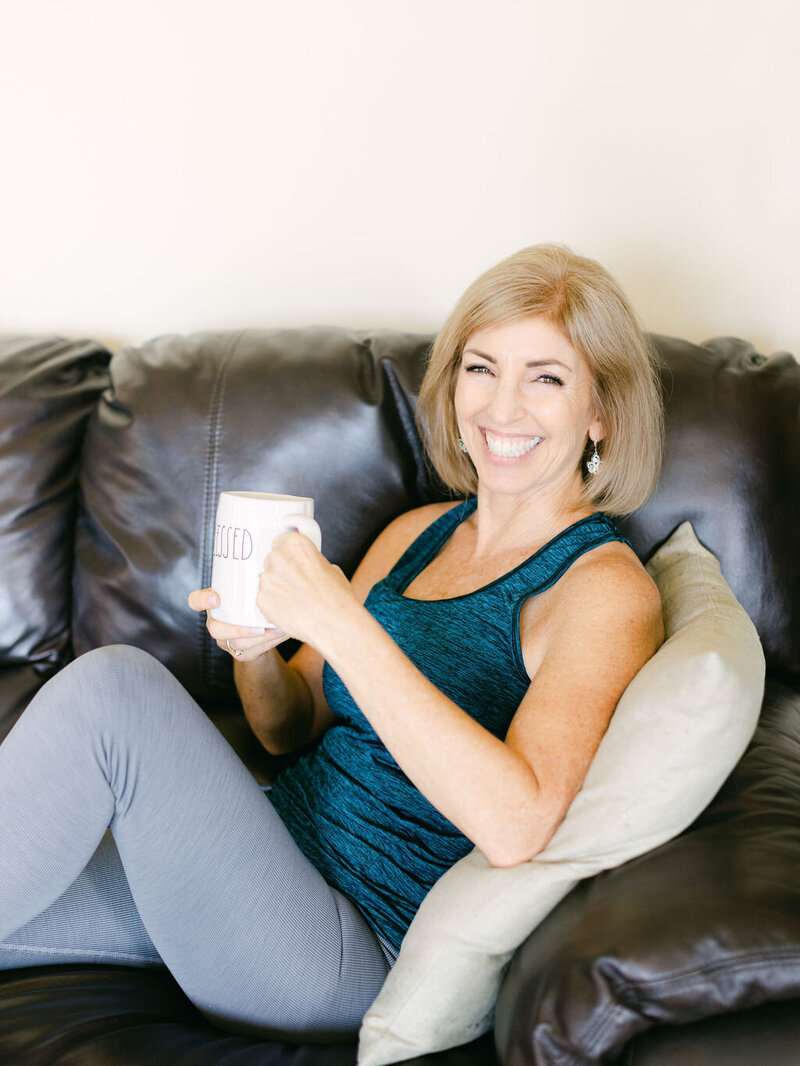 Lora Ulrich sitting comfortably on a couch with a cushion, holding a mug with the word 'JUICED,' enjoying a relaxed moment