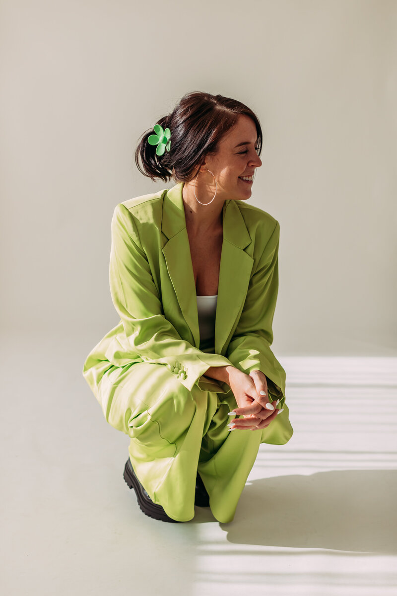 kneeling down for a branded photoshoot for studio seven fifteen in a green suit and smiling