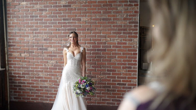 bride standing in front of brick wall while smiling and holding bridal bouquet