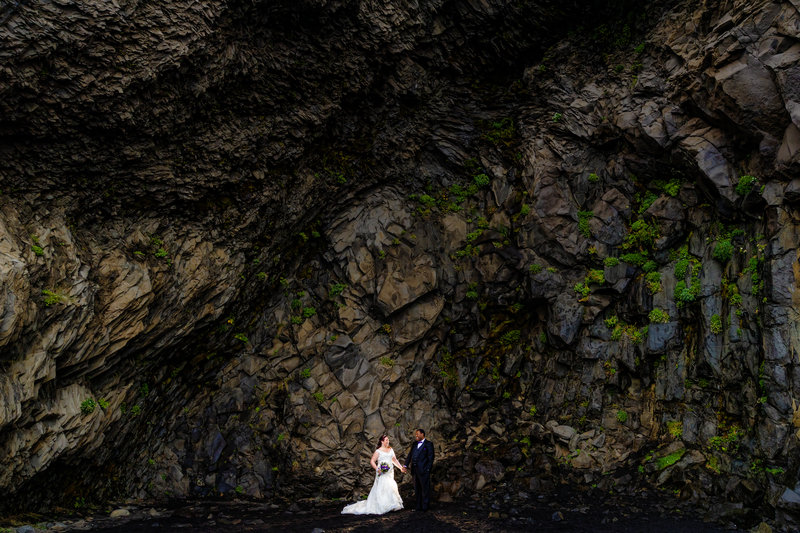 Bride and groom standing on a black sand beach in Iceland, surrounded by the dramatic and otherworldly landscape.