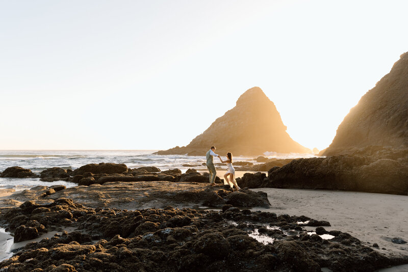 Groom helping bride up on the rocks during their Oregon Coast elopement.