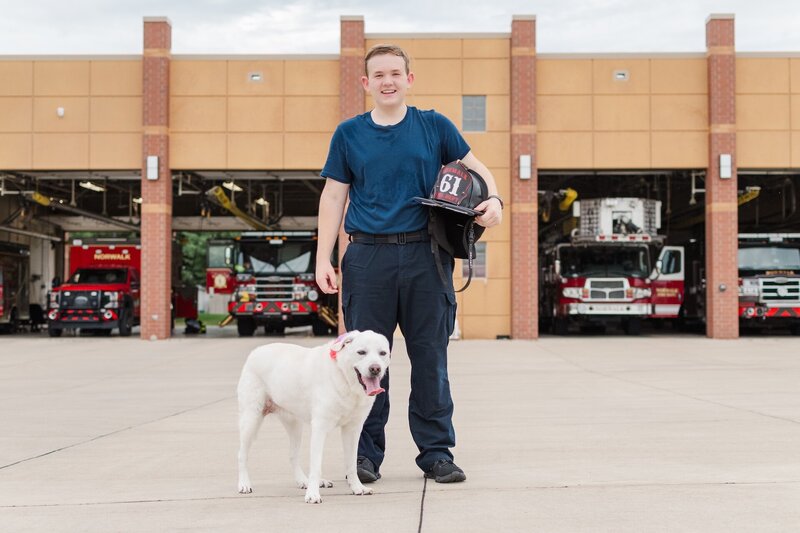 a high school grad standing at a fire station with his dog