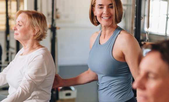 lead pilates instructor assisting two women on a reformer 