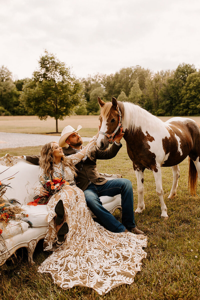 Bride and groom sitting down and petting a horse