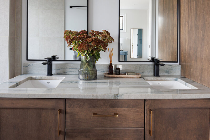 Double bathroom vanity in dark oak with a marble top and black faucet. There's a bouquet of flowers on the counters with soap tray and essence.