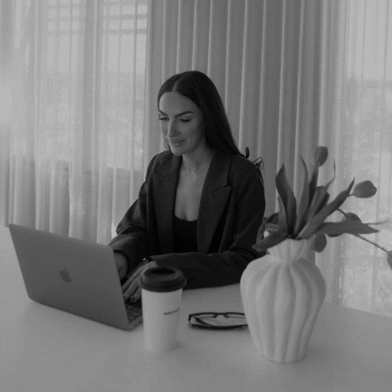 Woman working on laptop in a bright studio with coffee and glasses nearby, promoting a 5-page web design package delivered in one week