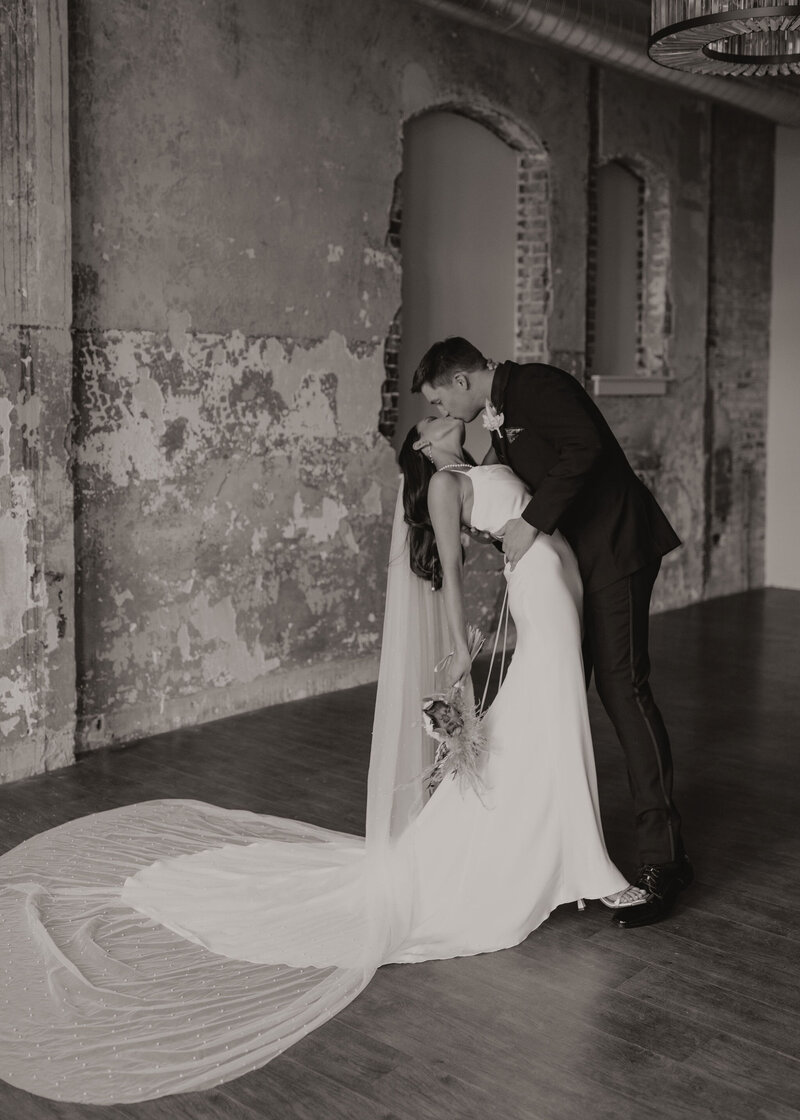 groom dips bride and kisses her in industrial brick room
