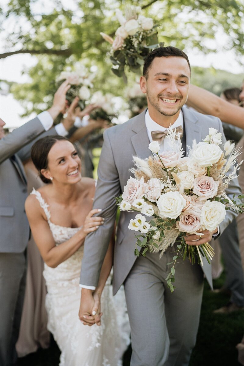 High end wedding couple holding hands and bouquet running through wedding party in Minnesota