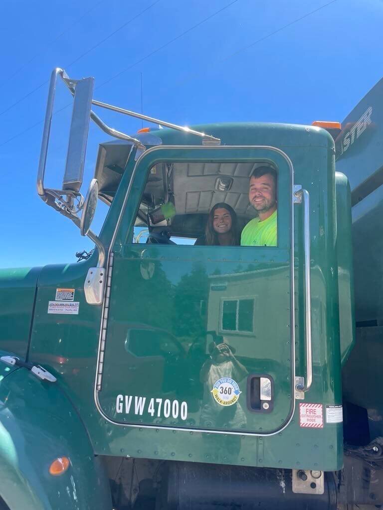 Katy and Steve smile from the cab of one of their garbage and recycling trucks in rural Lane County.