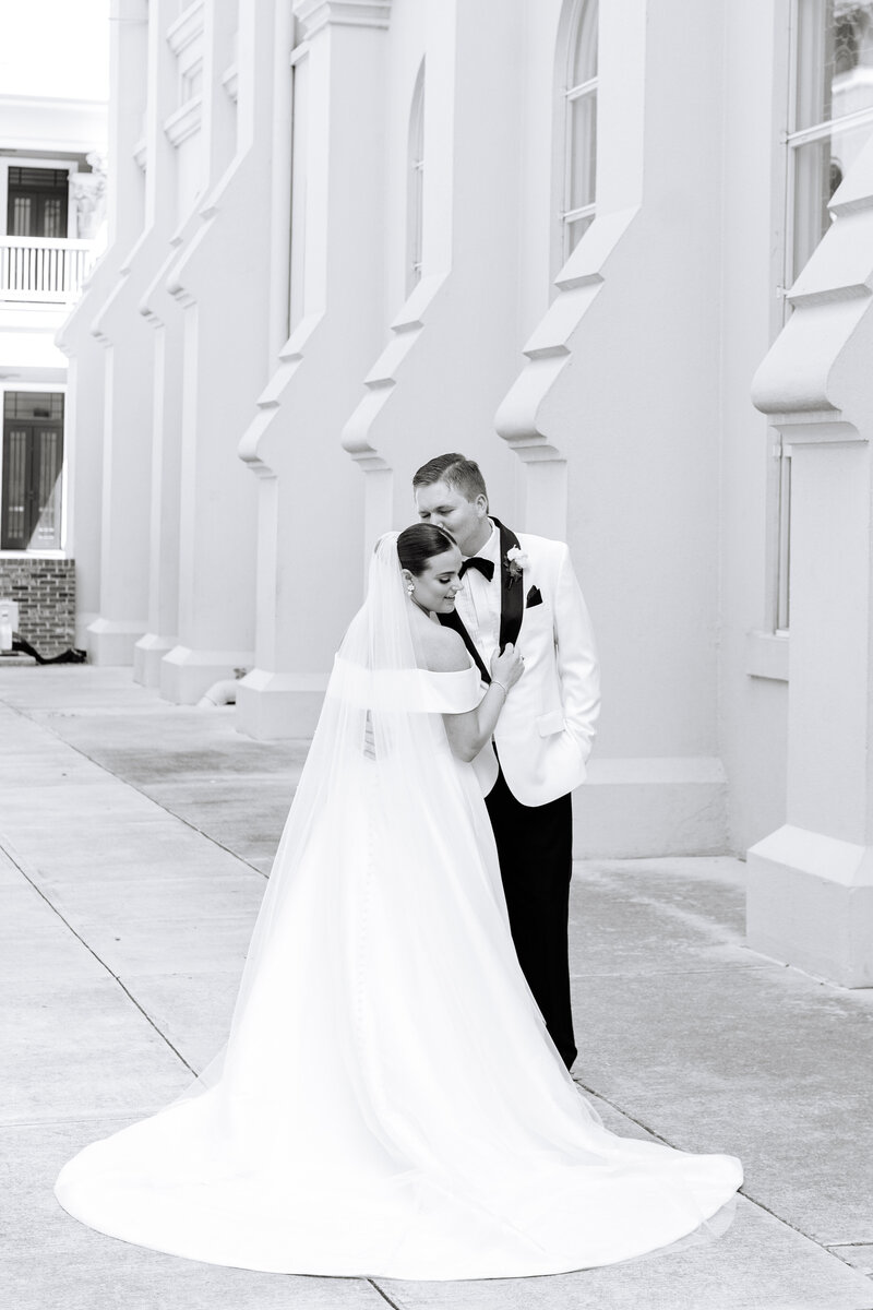 Black and white photo of bride and groom posing in front of large building