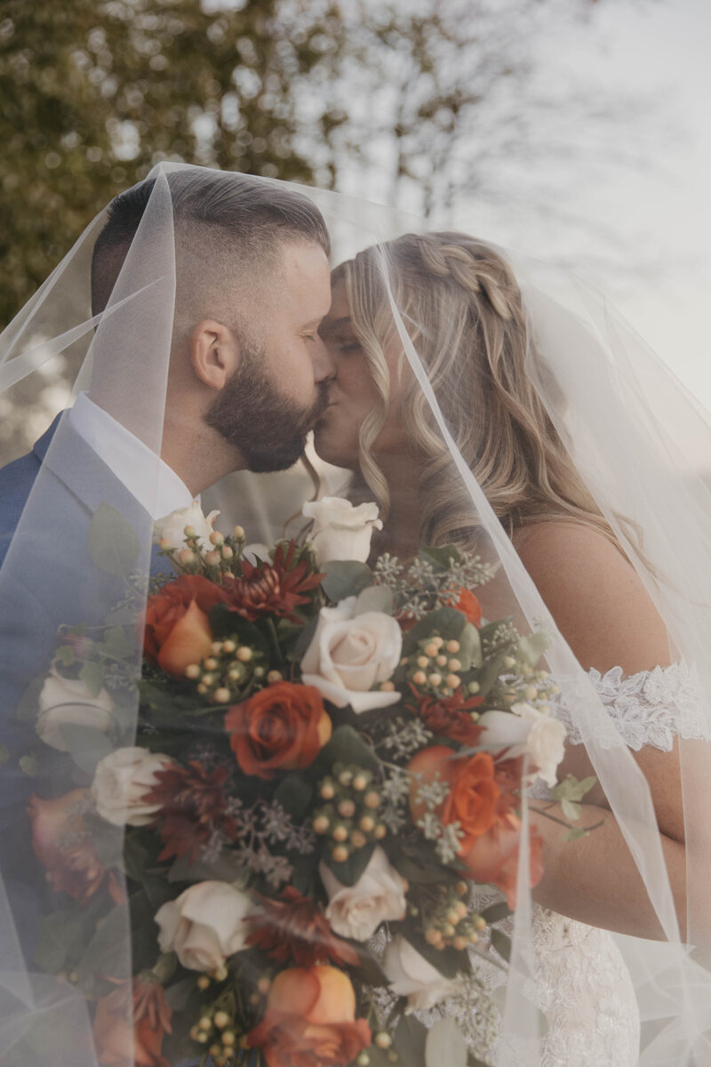 Bride and groom sitting kissing under a tree