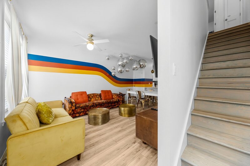 Colorful living area featuring a yellow sofa, vintage floral couch, and a ceiling of mirror balls under a bold retro stripe wall.