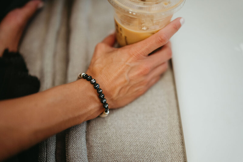 woman's arm holding iced coffee with bracelet that says "limitless"