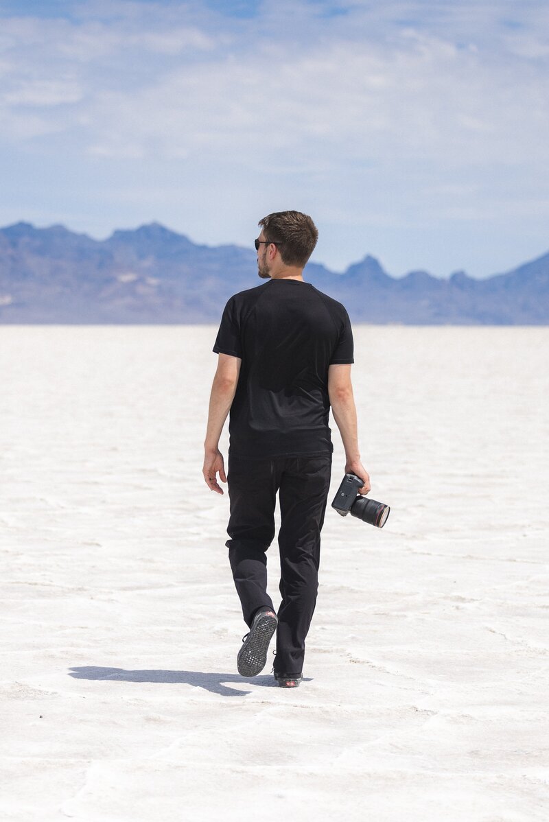 Man stands by the salt flats holding camera in Utah