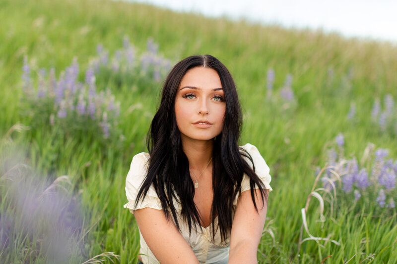 A young woman sitting in a field of purple wildflowers while looking forward.