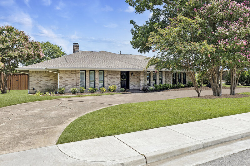 Charming brick ranch-style home with covered front porch, symmetrical windows, mature trees, and tiered walkway for curb appeal goals.