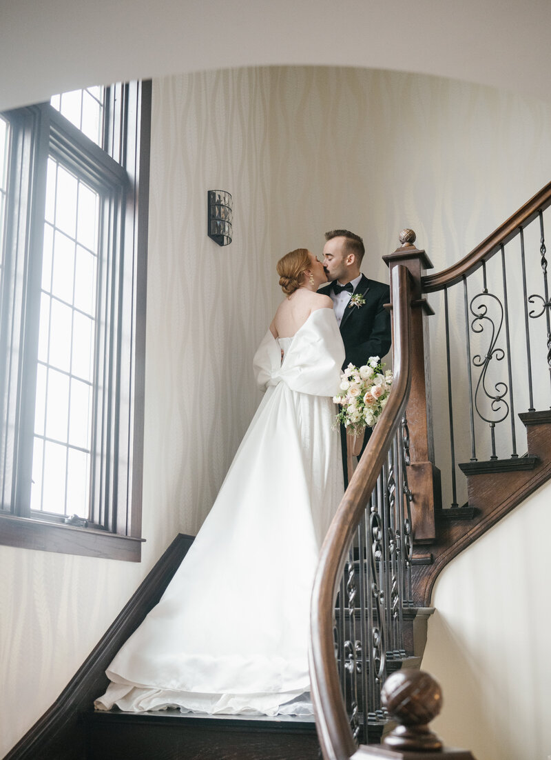 A bride and groom walk up a vintage staircase inside a manor in Michigan