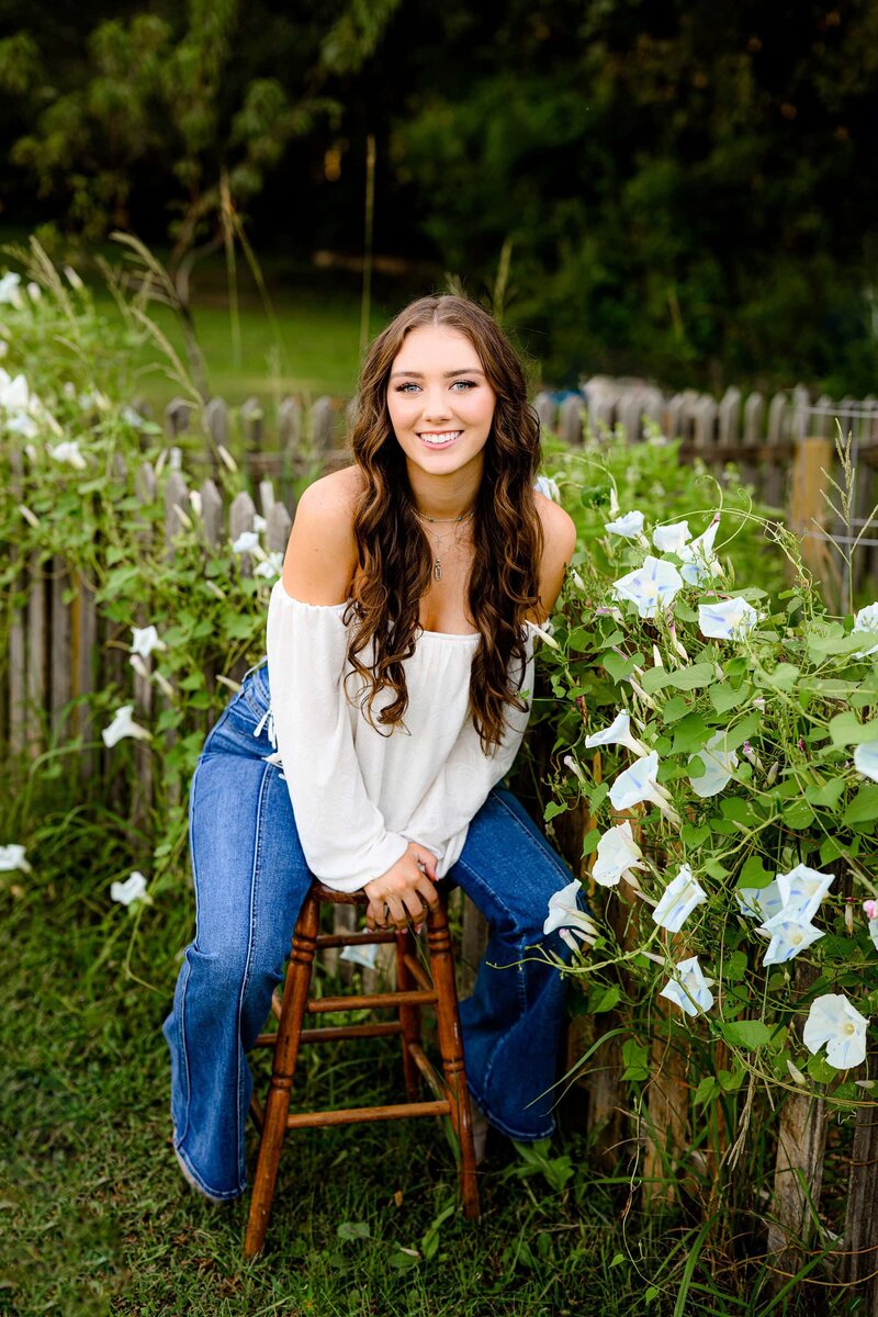 senior girl sits on stoll with flowers around her