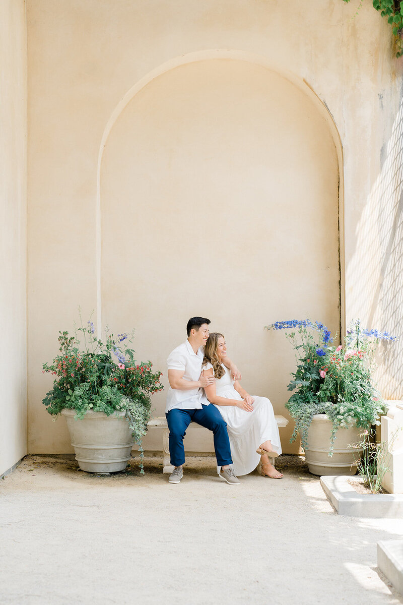 A couple sitting on a bench at Longwood Gardens during their engagement session.