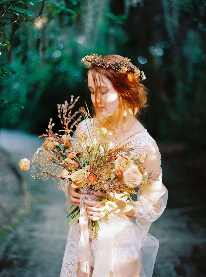 Woodland boudoir session with a floor-length lace bridal robe, peach bouquet with wispy flowers and a dyed texture flower crown