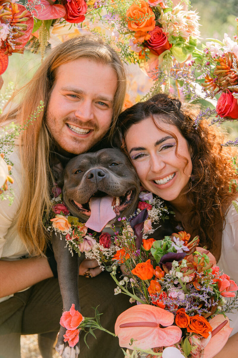 Bride and groom smiling with their dog surrounded by colorful florals during their Colorado mountain wedding.