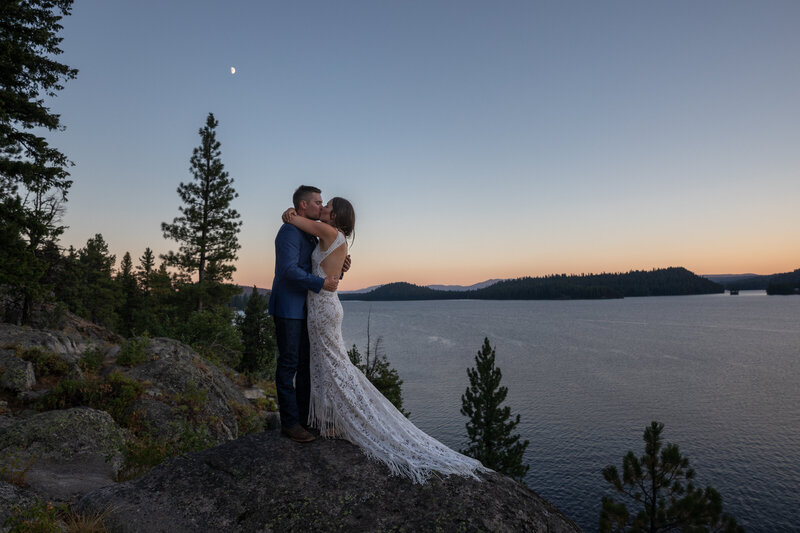 Newlyweds hug and kiss  after their first dance while on a rock above an Idaho lake at sunset.