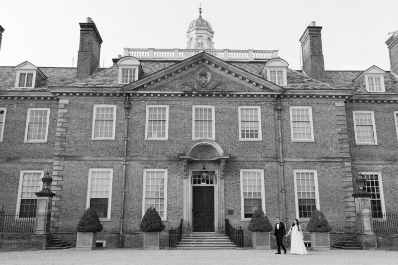 Black and white photo of a stately brick mansion with a bride and groom walking towards the front steps