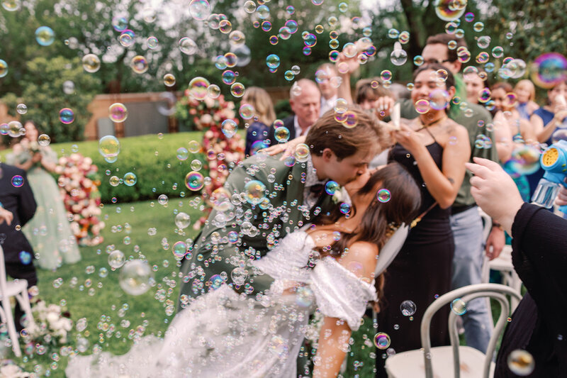 A couple does a dip kiss surrounded by bubbles after their wedding ceremony at Barr Mansion
