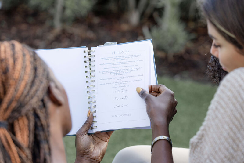 two women reading a promise contract from a fitness journal