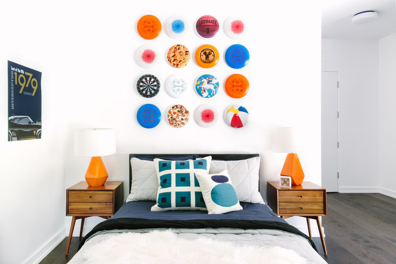 Orange, navy, and white modern boys bedroom with frisbee art, walnut night stands and orange table lamps.