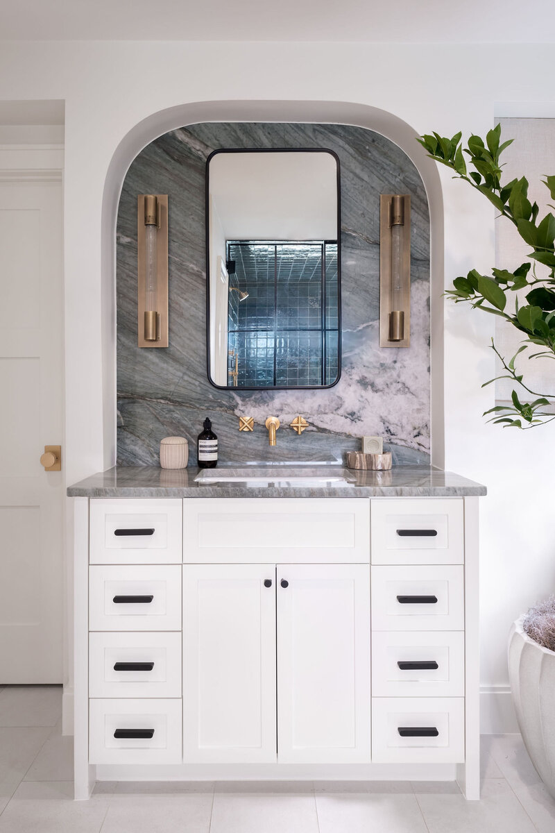 Warm wood Stain Primary Bathroom Vanity with Brass Arched Mirrors and Faucet and Sconces with Gray and White Mosaic Marble Floors