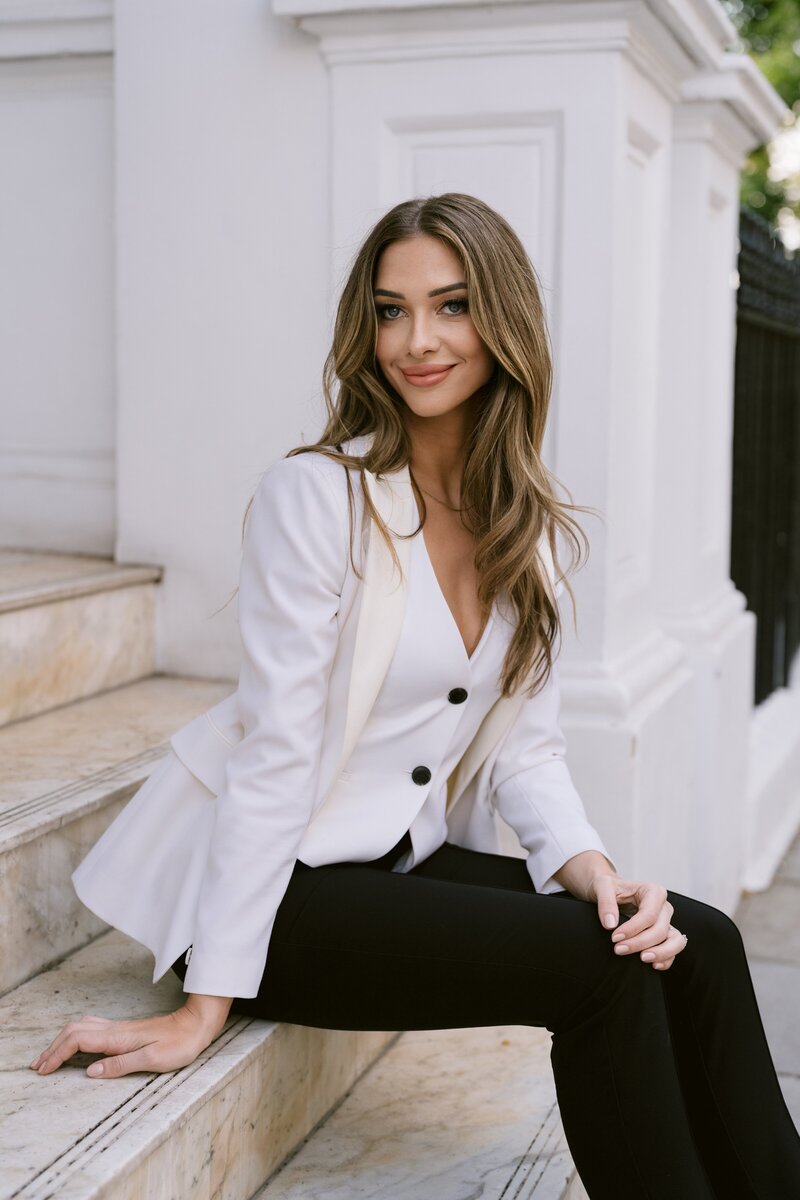 Black and white image of Melinda Gill, Founder and CEO of Luxus Events, in Mayfair, London, holding a book in a stylish white outfit.
