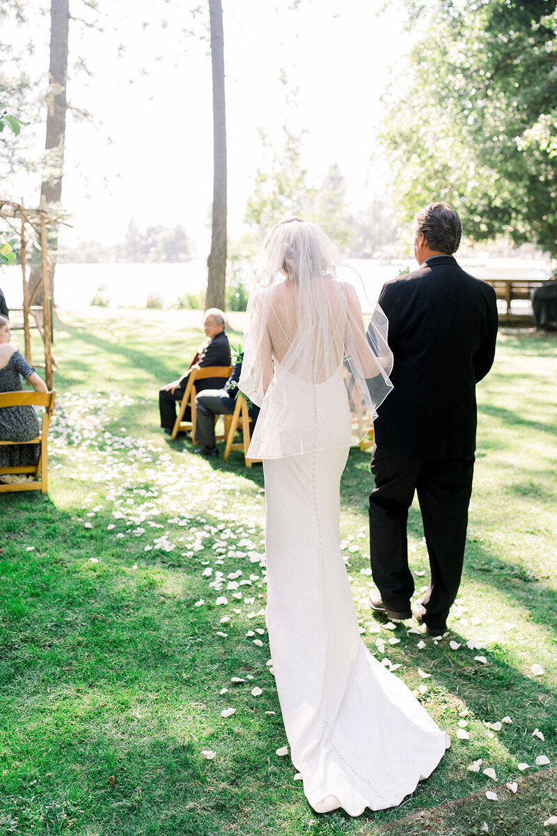 Tiffany Longeway Photography captures a serene moment as the bride walks down the aisle with her father at The Boathouse at River Highlands Ranch in Smartsville, California. Surrounded by the natural beauty of the lakeside setting and the soft glow of sunlight filtering through the trees, this image reflects the intimate and picturesque atmosphere of a lakeside wedding. Ideal for couples seeking a tranquil and beautiful venue for their special day.