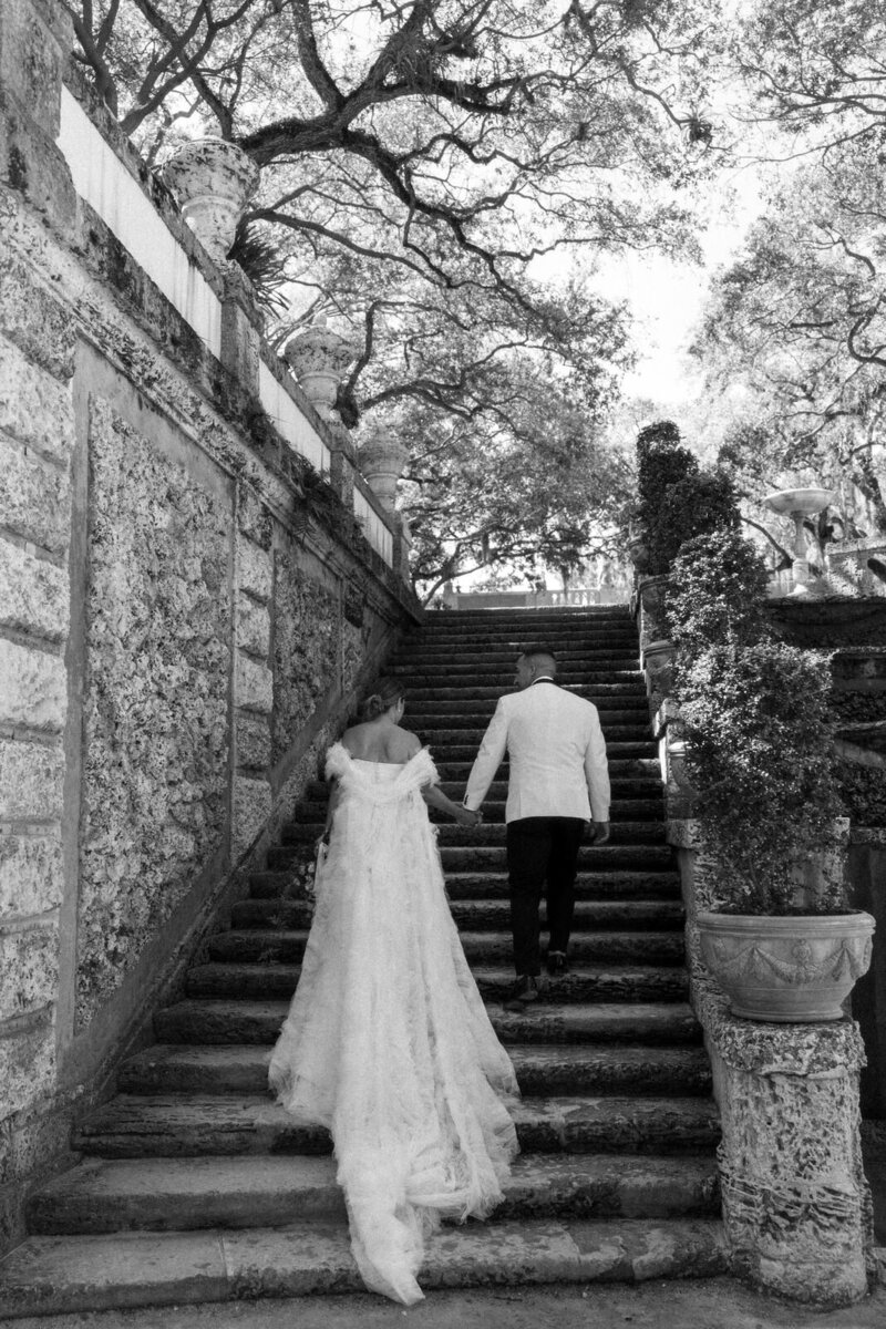 Bride and groom walking up stairs at Vizcaya Museum with the Bride's cape trailing behind her in Miami FL, photographed by Andrea-Marie Photography