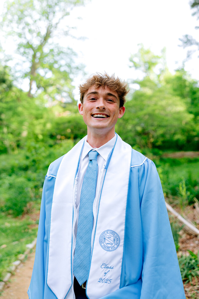 College graduate smiling outdoors during a spring portrait session.