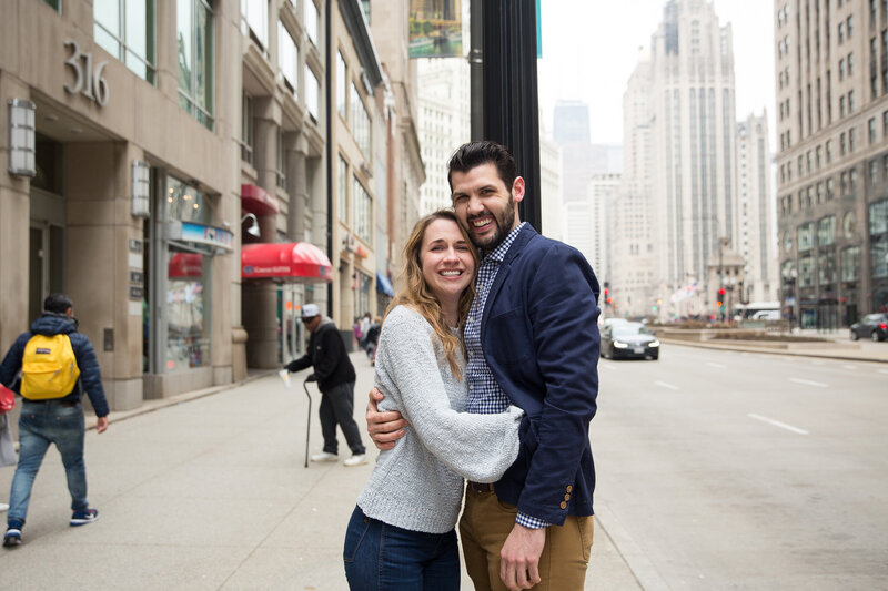 couple hugging after surprise proposal woman gasping from surprise engagement downtown chicago mag mile
