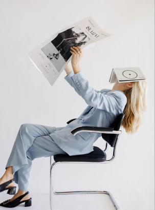 A blonde woman sitting in a chair with a book over her face reading the newspaper 