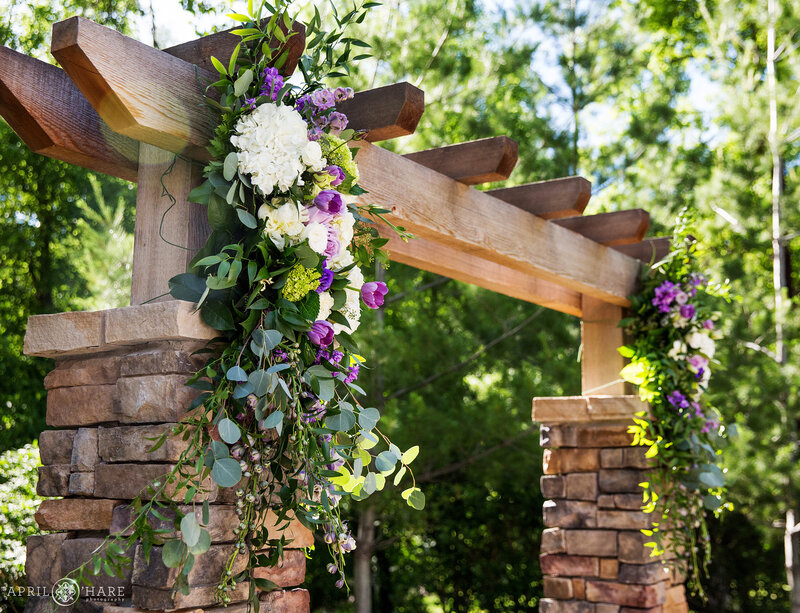 Purple florals decorate the terrace stone arch on the ceremony lawn at Boulder Creek Wedgewood Weddings in Colorado