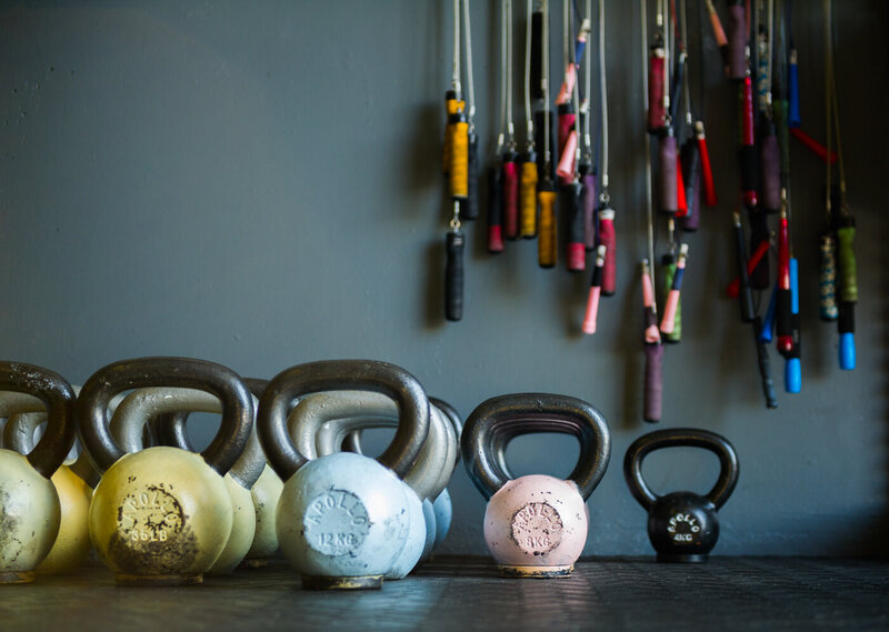 Rows of kettle bells lined up on the floor and jump ropes hanging on the wall behind.