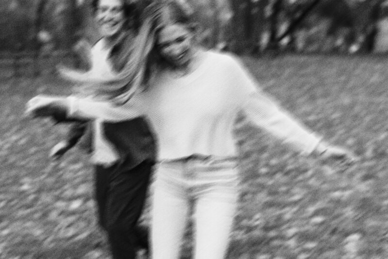 black and white image of two women running through a field with fallen leaves on the ground and motion blur from their joyous movement photographed by minnesota photographer tom thornton photography